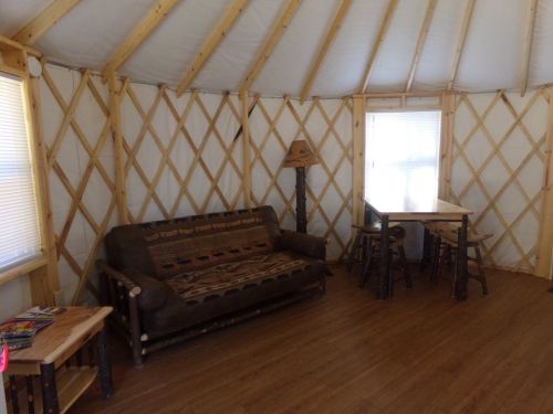 Interior of a yurt featuring a sofa, table, and wooden stools, with natural light from a window.
