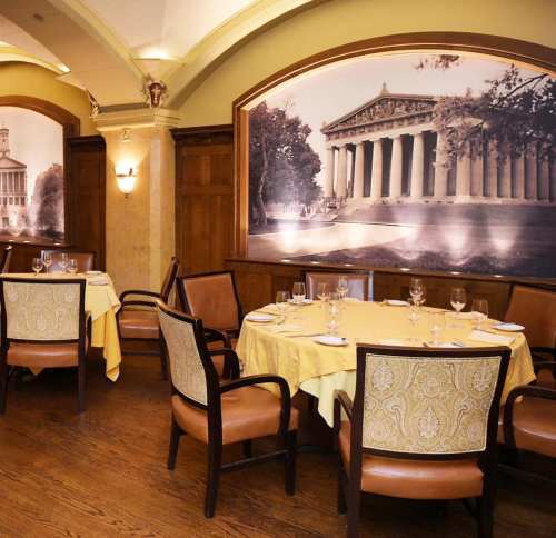 Elegant restaurant interior with yellow tablecloths, wooden accents, and large historical wall murals.