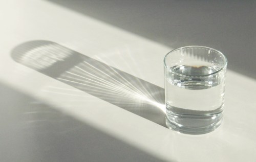 A clear glass of water casting intricate shadows on a light surface.