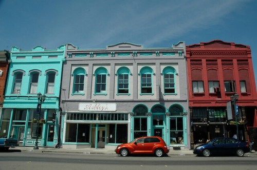 Colorful historic buildings line a street, featuring turquoise, gray, and red facades with shops and parked cars.