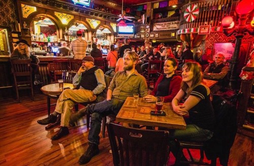 A lively bar scene with patrons seated at tables, enjoying drinks and watching a performance in a vibrant atmosphere.