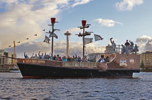 A pirate-themed boat with people waving, sailing on water with the Seattle Space Needle in the background.