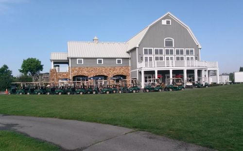 A large gray building with a stone base, surrounded by green grass and lined with golf carts. Clear blue sky above.