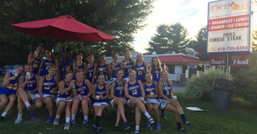 A group of female basketball players poses together outside a restaurant, celebrating with thumbs up and smiles.