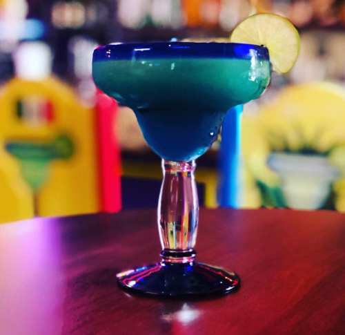 A vibrant blue margarita in a decorative glass, garnished with a lime slice, on a wooden table.