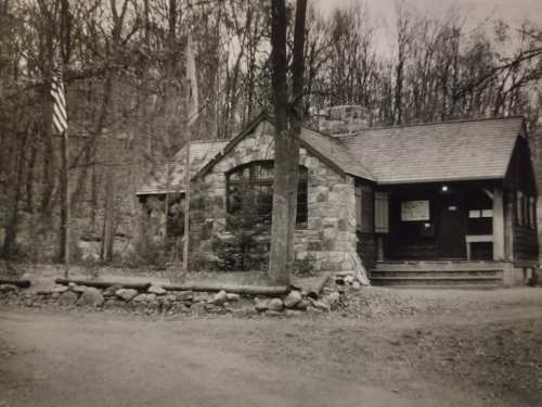 A rustic stone building surrounded by trees, featuring a flagpole and a pathway leading to the entrance.