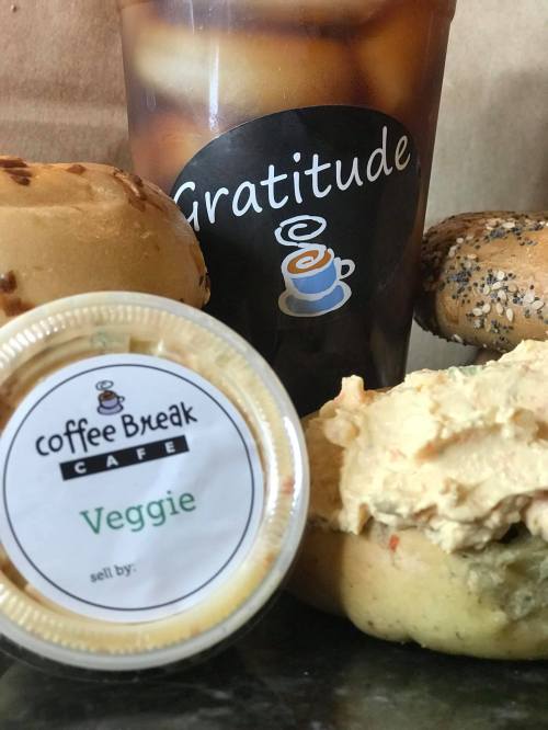 A cup of iced coffee next to a veggie spread and bagels on a table, with a "Gratitude" logo on the cup.