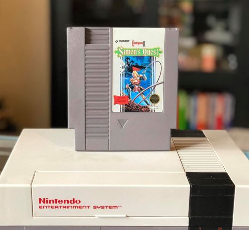 A classic Nintendo Entertainment System cartridge for "Simon's Quest" resting on the console.