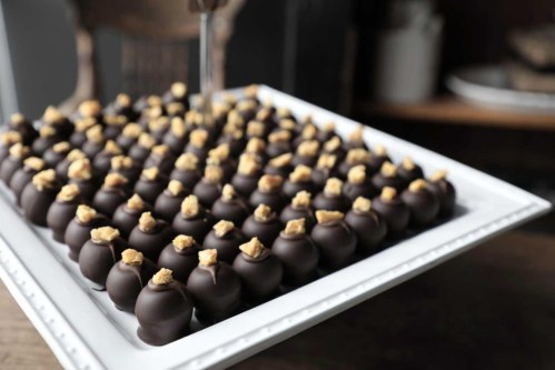 A white platter filled with rows of chocolate-covered treats topped with small pieces of cookie.