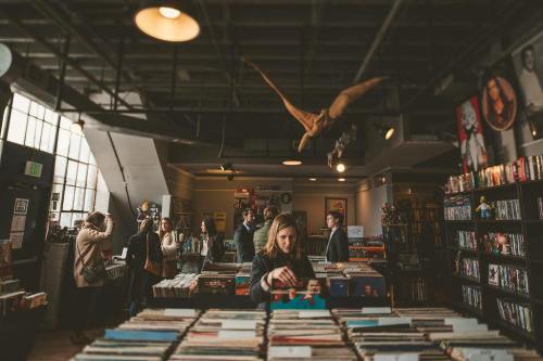 A woman browses vinyl records in a cozy store filled with people and colorful decor.