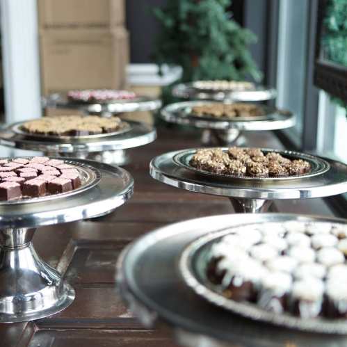 A display of assorted desserts on silver trays, featuring cookies and treats, set on a wooden table.