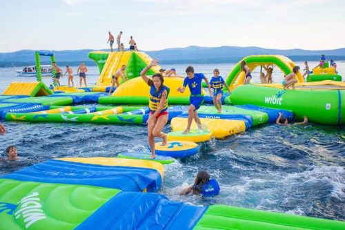 A vibrant water park with inflatable structures, where people are playing and jumping in the water on a sunny day.