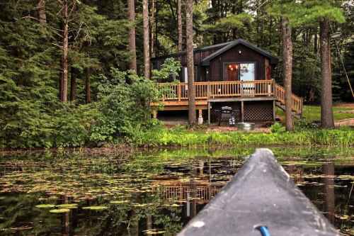 A cozy cabin surrounded by trees, reflecting in a calm pond, viewed from a canoe.