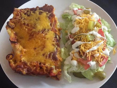 A plate with cheesy lasagna and a fresh salad topped with lettuce, tomatoes, pickles, and shredded cheese.