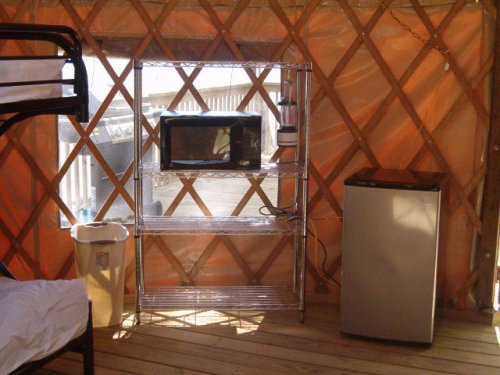 Interior of a yurt featuring a bunk bed, a shelf with a microwave, and a small refrigerator.