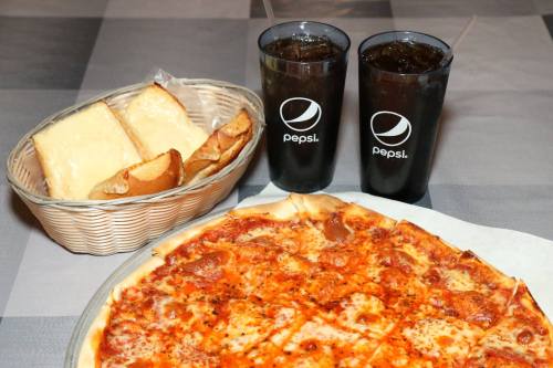 A pizza with pepperoni, two glasses of Pepsi, and a basket of breadsticks and cheese on a table.