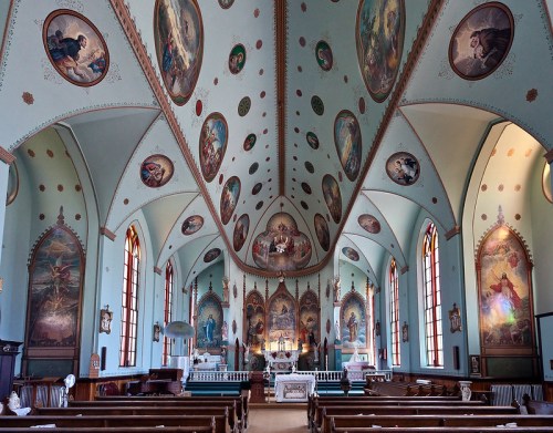 Interior of a beautifully decorated church with colorful murals, arched ceilings, and wooden pews.