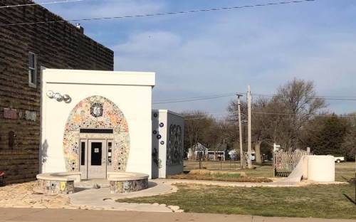 A colorful, mosaic-decorated building with a curved entrance, surrounded by grass and a playground area.
