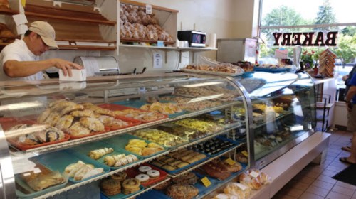 A bakery display case filled with various pastries, while a baker prepares orders behind the counter.