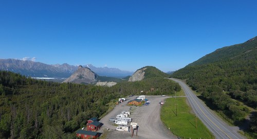 A scenic view of a highway with RVs parked, surrounded by mountains and clear blue skies.