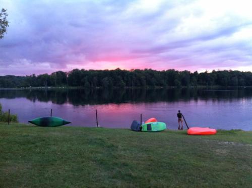 A serene lake at sunset, with colorful kayaks on the shore and a person preparing to launch a kayak into the water.