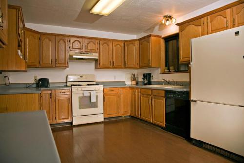 A spacious kitchen with wooden cabinets, a white stove, and a black dishwasher, featuring a simple countertop and overhead lighting.