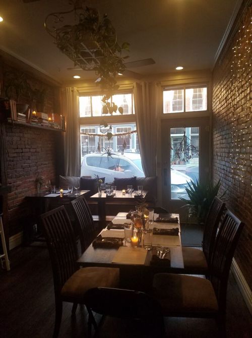 Cozy restaurant interior with wooden tables, soft lighting, and large windows overlooking the street.