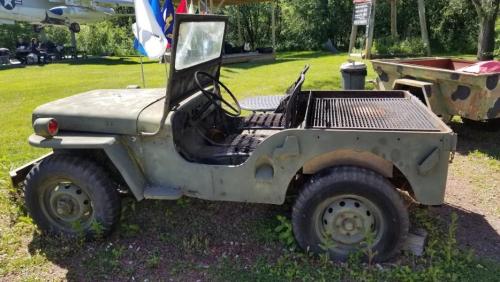An old military jeep parked on grass, featuring a rusty exterior and an open cargo area.