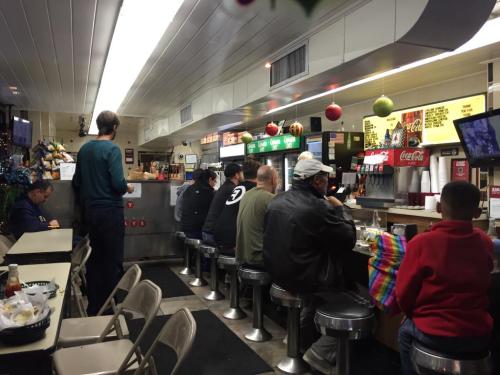 A diner scene with patrons sitting at a counter, enjoying food and drinks, with festive decorations overhead.