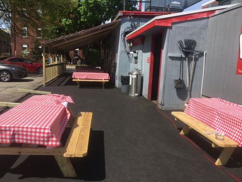 Outdoor dining area with picnic tables covered in red and white checkered tablecloths, surrounded by a wooden shelter.