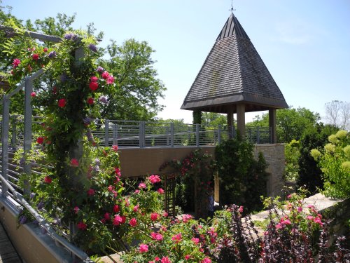A garden scene featuring vibrant flowers and a wooden pavilion with a pointed roof under a clear blue sky.