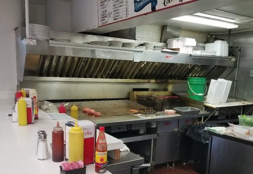 A restaurant kitchen with a grill, condiments, and plates, showcasing a clean and organized cooking area.