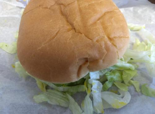 A plain sandwich bun resting on shredded lettuce, placed on a piece of parchment paper.