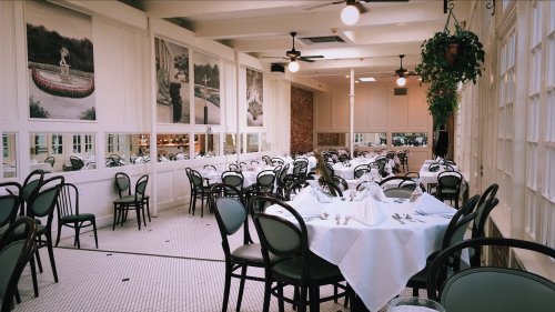 A spacious restaurant interior with white tables, black chairs, and large windows, featuring decorative wall murals.
