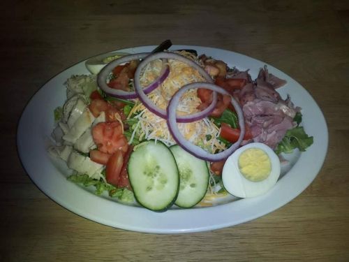 A colorful salad with lettuce, tomatoes, cucumbers, sliced meats, cheese, red onions, and a hard-boiled egg on a plate.