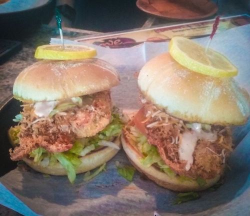 Two stacked chicken sandwiches with lettuce, sauce, and lemon slices, served on a tray with colorful toothpicks.