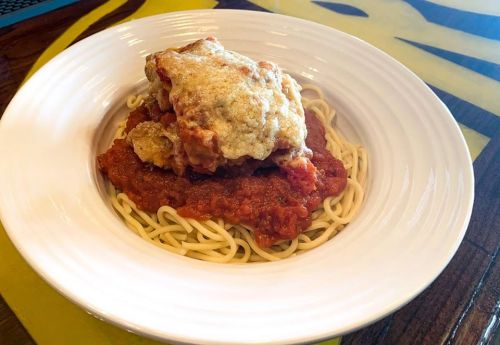 A plate of spaghetti topped with marinara sauce and a breaded chicken cutlet.