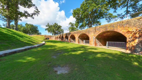 A grassy area with a brick archway structure surrounded by trees and blue skies.
