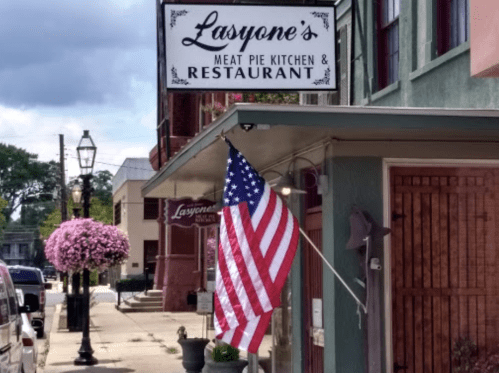 Sign for Lasyone's Meat Pie Kitchen & Restaurant, featuring an American flag and hanging flowers outside.