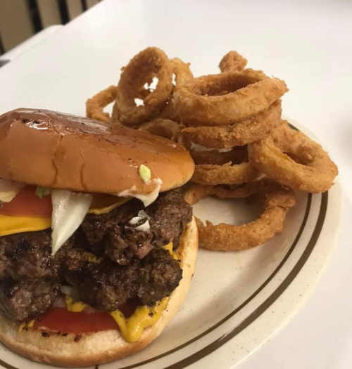 A juicy double cheeseburger with cheese, onions, and tomato, served with a side of crispy onion rings.