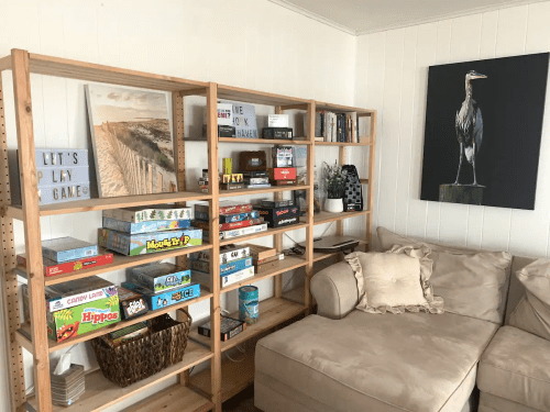 A cozy living room with a bookshelf filled with board games and a large painting of a heron on the wall.