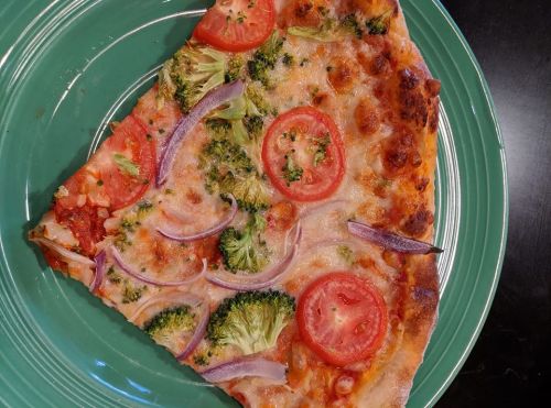A slice of pizza topped with broccoli, tomatoes, and red onions on a green plate.