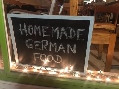 A chalkboard sign in a window reads "Homemade German Food," surrounded by string lights.