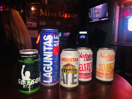 A table with various beer cans, including Lagunitas and Natural Light, in a dimly lit bar setting.