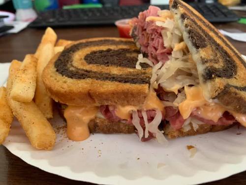 A close-up of a sandwich with layers of meat, sauerkraut, and cheese on marbled rye, served with fries on the side.