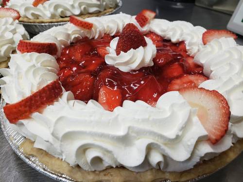 A close-up of a strawberry pie topped with whipped cream and fresh strawberries, featuring a glossy red glaze.