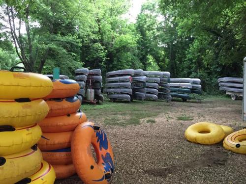 A stack of gray kayaks and yellow inflatable tubes in a wooded area, with trees surrounding the storage space.