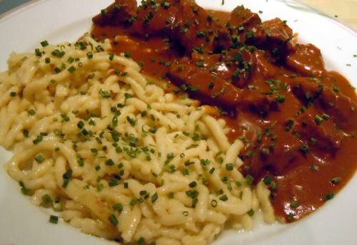 A plate of tender meat in rich sauce served with creamy pasta, garnished with chopped chives.
