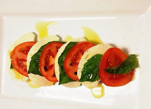A plate with layered slices of mozzarella, tomatoes, and fresh basil drizzled with olive oil.