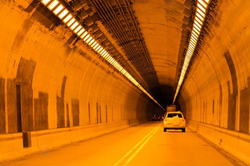A view of a long, illuminated tunnel with vehicles driving through, featuring warm orange lighting and concrete walls.